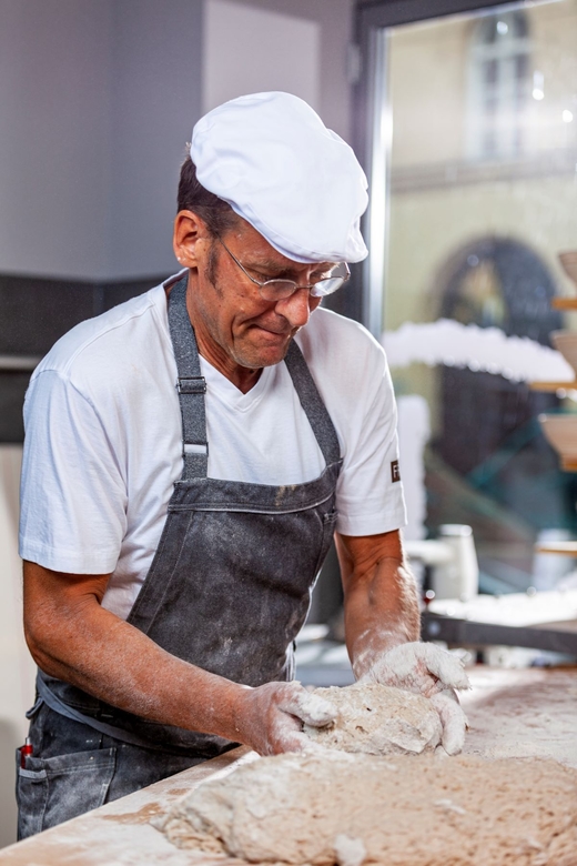 Mann in Bäckerkleidung knetet Teig auf einer Arbeitsplatte